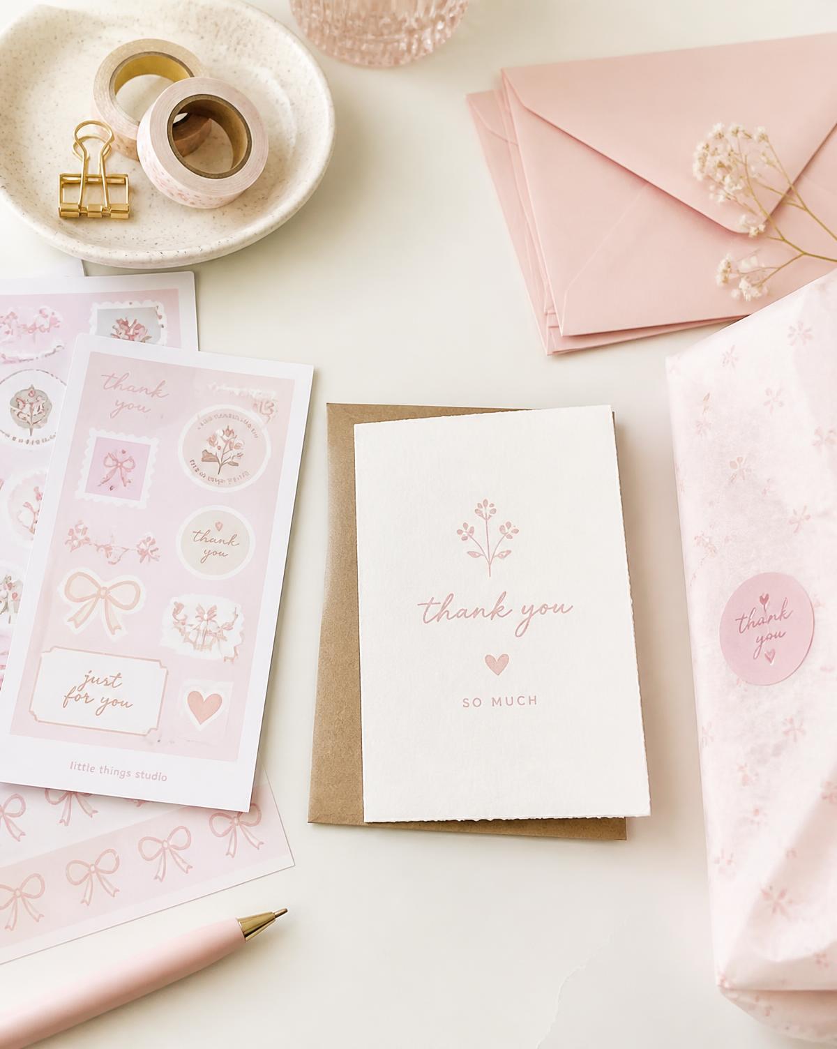 Pink sticker sheets, blush envelopes and a hand-stamped thank-you card on a cream desk